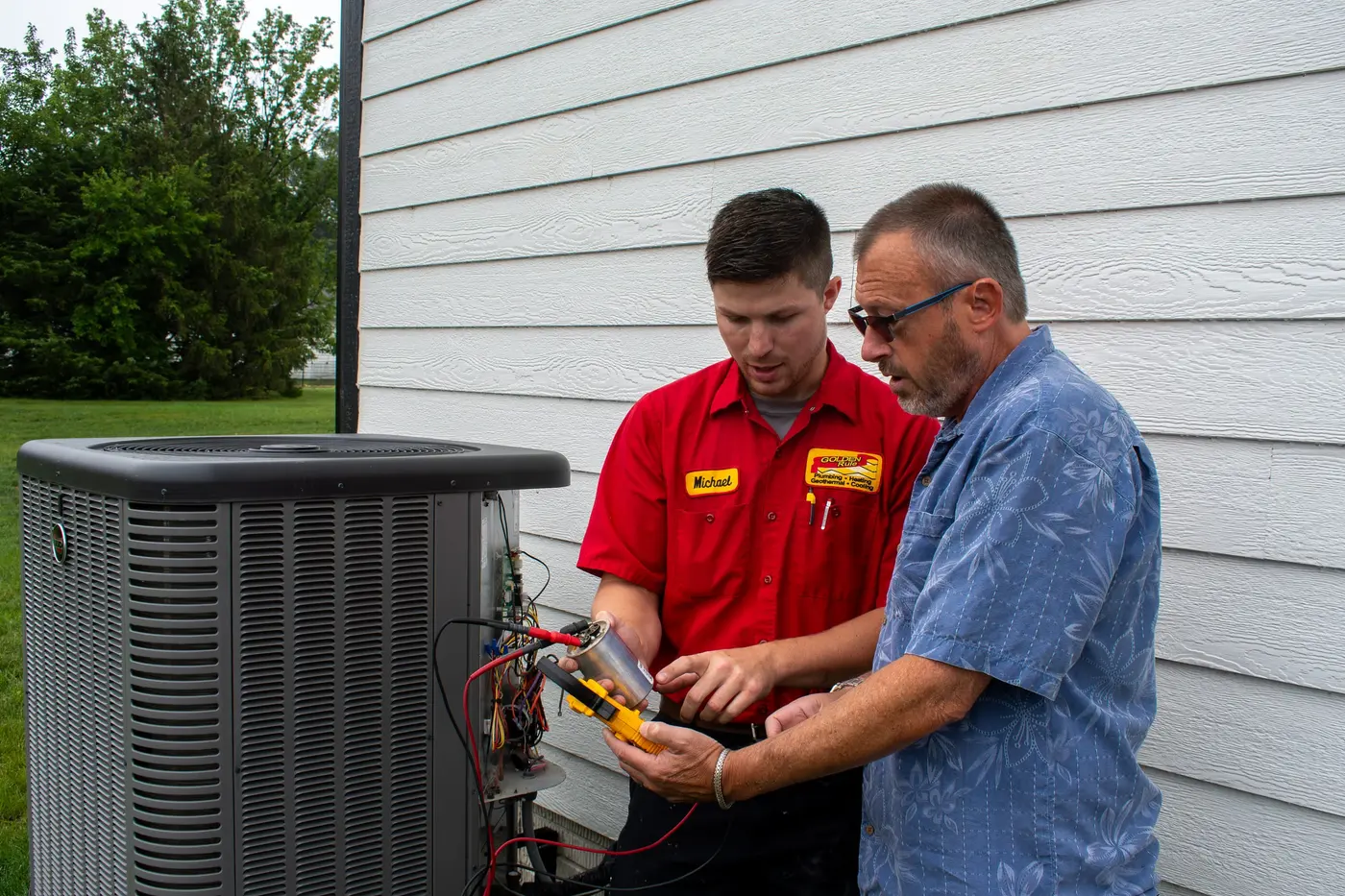 A Golden Rule technician showing a homeowner the outdoor air conditioner beside their Utah home