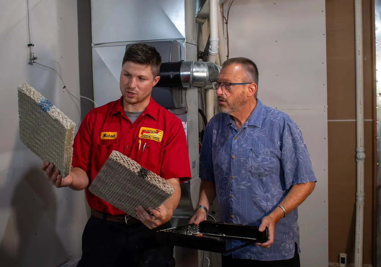 A Golden Rule technician showing a homeowner an old humidifier pad next to a new one