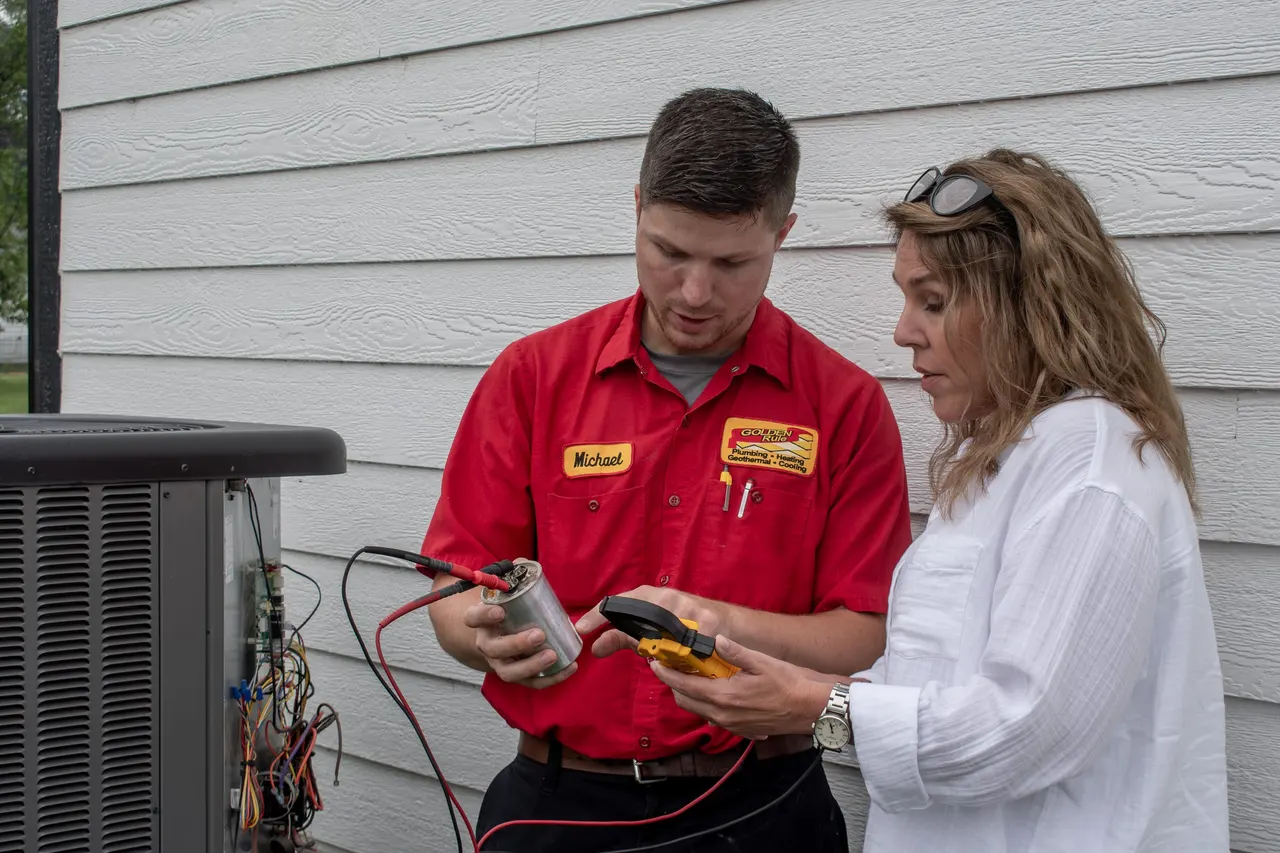 A Golden Rule technician showing a homeowner a part from their outdoor AC unit