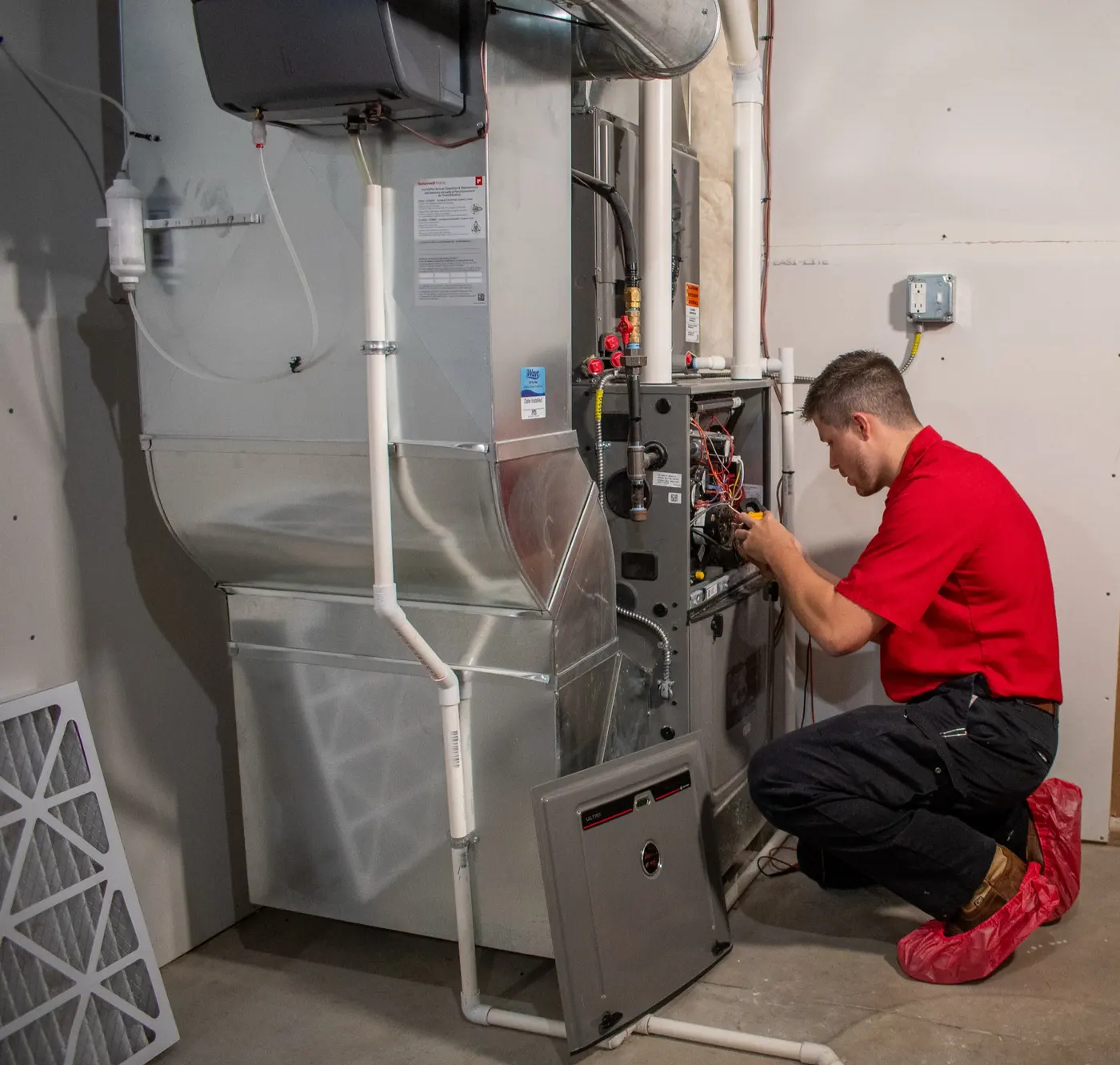 A Golden Rule technician in shoe covers servicing a furnace in a Utah basement