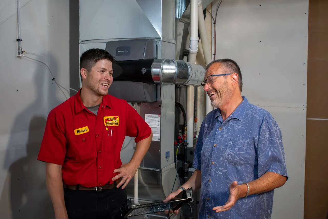 A Golden Rule technician talking with a homeowner in front of their furnace