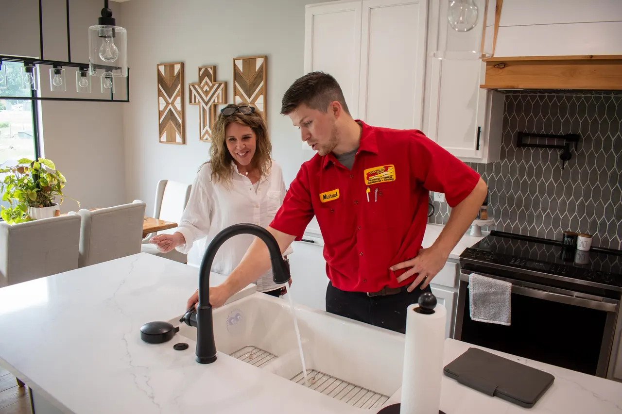 A Golden Rule plumber checking a kitchen faucet with a homeowner