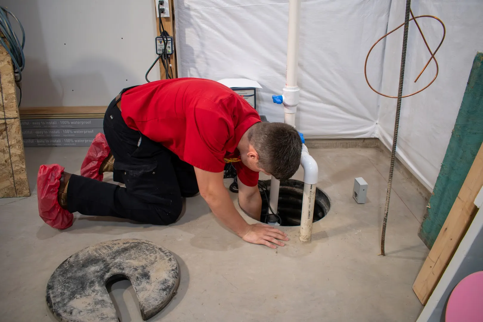 A Golden Rule technician in shoe covers servicing a sump pump inside a customer's basement