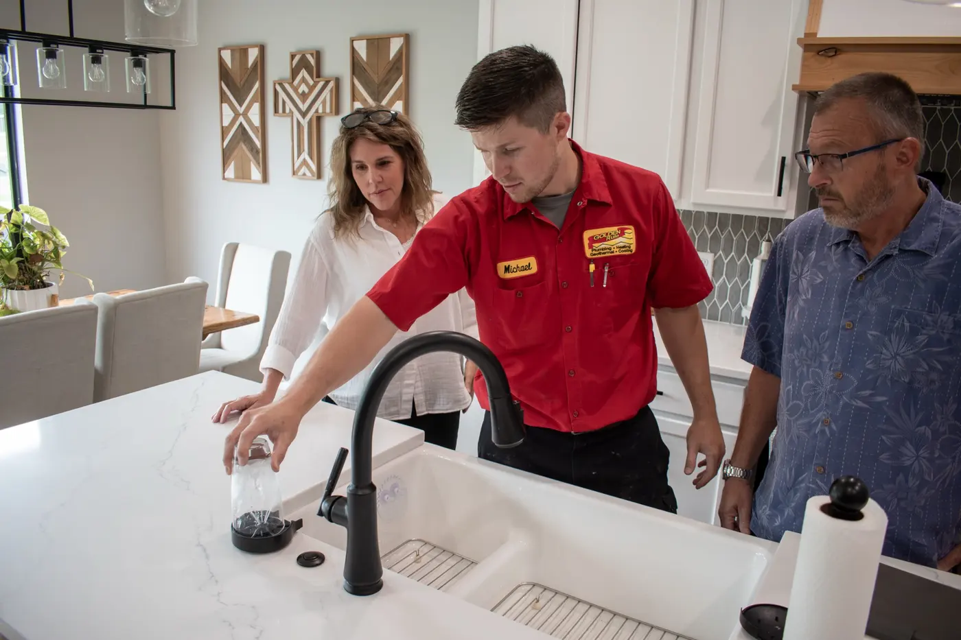 A Golden Rule technician testing water at a kitchen sink while the homeowners watch